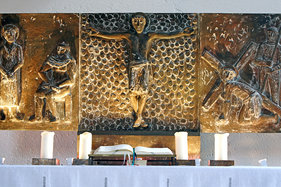 Bronze-Relief der Passion auf Altar, Künstler Fritz Fleer, unten 4 Kerzen neben offener Bibel, gelbe Strahler ein